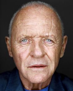 an older man in a blue suit and tie looking at the camera with a serious look on his face