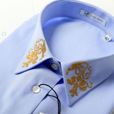 The office blue shirt with golden floral embroidery on the collar and cuffs made by ALISIA ENCO. Grandeur blue shirt. ALISIA ENCO is a fashion brand for businesswomen built around already iconic shirts, a business that sets to inspire women and ignite their creativity in life. Grandeur shirt collection is about the elegance of the traditional symbols embroidered on the collar and cuffs: gold thread on the finest of fabrics for a gorgeously elegant look. The Romanian traditional motifs enriching this collection provide a splendid paradox: its details are subtle but somehow they never get unnoticed. Enjoy the Grandeur Collection as it instills creative traditional motifs into the sobriety of a business shirt for an outstanding appearance speaking of excellence and creativity. Each shirt of t Formal Long Sleeve Blouse With Embroidered Cuffs, Formal Long Sleeve Tops With Embroidered Cuffs, Elegant Gold Formal Tops, Elegant Gold Tops For Formal Occasions, Elegant Long Sleeve Embroidered Shirt, Elegant Tops With Embroidered Cuffs, Formal Fitted Tops With Embroidered Cuffs, Traditional Embroidered Shirt For Formal Occasions, Elegant Embroidered Formal Tops