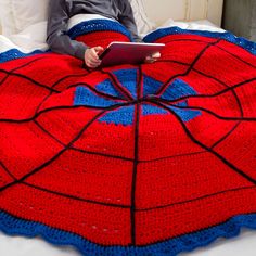 a person laying in bed with a red and blue blanket on top of it, holding a tablet