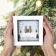 someone holding up a christmas ornament with three rocks in front of a tree