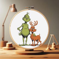 the grin and the deer cross stitched together in an embroidery hoop on a wooden table