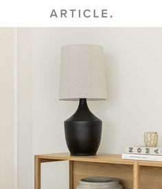 a black lamp sitting on top of a wooden table next to a white vase and book