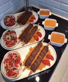 several plates with food on them sitting on a stove top next to dipping sauces