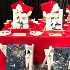 two santa hats sitting on top of a red table covered in paper plates and paint