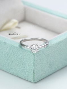 a white gold ring with a single diamond in it's box on a table