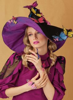 a woman wearing a purple hat with butterflies on the side and her hands under her chin