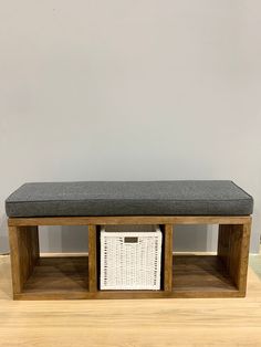 a wooden bench with two baskets underneath it on the floor in front of a gray wall