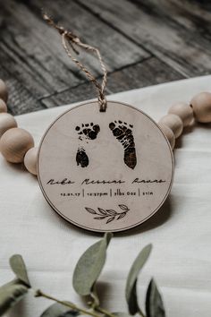 a wooden beaded necklace with two baby footprints on it and an olive branch next to it