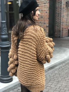 a woman is walking down the street wearing a brown sweater and black hat with her hands in her pockets