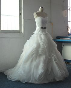 a white wedding dress is on display in front of a window and blue carpeted floor