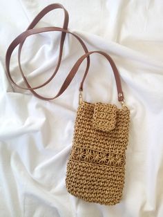 a crocheted purse sitting on top of a white bed next to a brown strap