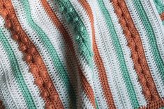 an orange and white crocheted blanket is laying on a bed with green trim