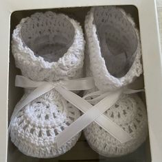 two pairs of white crocheted baby shoes in a box with ribbon around the ankles