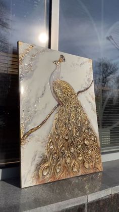 a white and gold peacock painting sitting on top of a counter next to a window