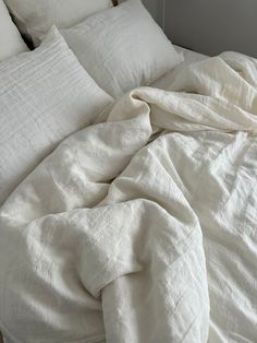 an unmade bed with white sheets and pillows