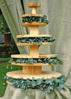 a three tiered cake stand with greenery on the bottom and green leaves on top