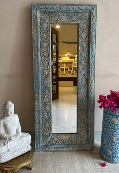 a mirror sitting next to a vase with flowers in it and a buddha statue on the floor