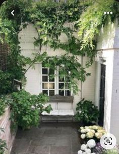 a white bench sitting in the middle of a garden next to a building with lots of greenery on it