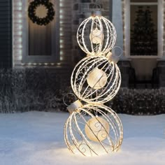 a christmas tree made out of wire and balls in the snow with lights on it