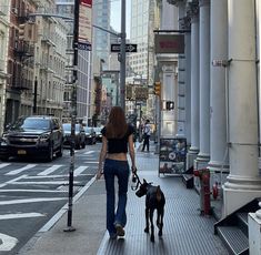 a woman is walking her dog down the sidewalk in front of tall buildings on a city street