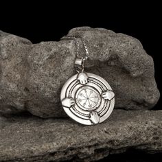 a silver pendant with an image of a compass on it sitting on top of a rock