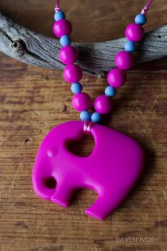 a pink elephant necklace with blue beads on a wooden table