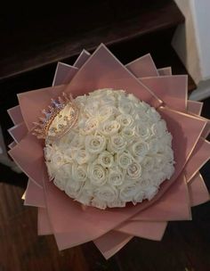 a bouquet of white roses with a diamond ring on top in pink paper wrapped around it