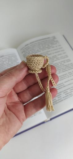 a hand holding an open book with a crocheted tassel on top of it