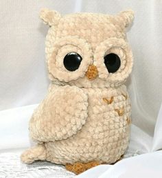 an owl stuffed animal sitting on top of a white bed sheet with eyes wide open