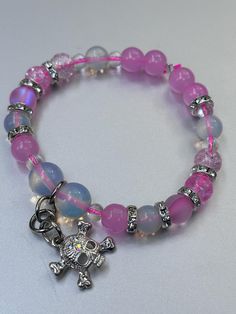 This stunning Opalite bracelet features a vibrant mix of pink beads, complemented by a unique charmed skull for a touch of edgy elegance. Opalite, known for its serene and calming energy, enhances personal power and emotional balance. It is believed to improve communication, clear mental blockages, and help with transitions, making it a perfect companion for navigating life's changes. The soft, iridescent glow of Opalite symbolizes purity and spiritual growth, while the pink beads add a gentle, Adjustable Pink Rosary Bracelet With 8mm Beads, Adjustable Pink Charm Bracelet With 8mm Beads, Trendy Pink Beaded Charm Bracelet, Pink Charm Bracelet With 8mm Beads, Pink Charm Bracelet With Round Beads For Friendship, Pink Round Beads Charm Bracelet For Friendship, Pink Beaded Charm Bracelet, Pink Rosary Bracelet With Colorful Round Beads, Adjustable Pink Rosary Bracelet With Colorful Beads