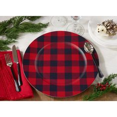 a red and black plaid dinner plate with silverware on the side next to pine branches