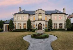 a large white house with lots of windows and bushes on the front lawn at dusk