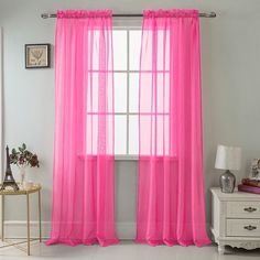 pink sheer curtains hanging on the side of a window in a room with white walls