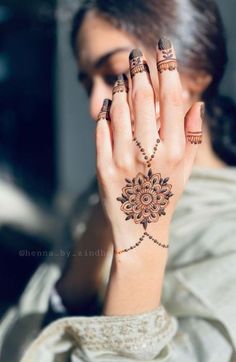 a woman holding her hand up to her face with henna tattoos on it's hands