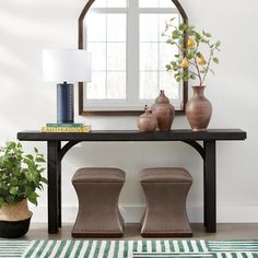 a table with two stools and a mirror on the wall above it, in front of a potted plant