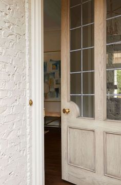 an open door to a white brick building with wood floors and glass panels on the doors