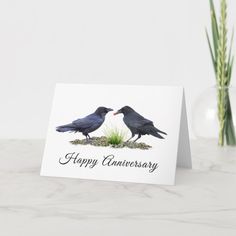 two black birds sitting on top of each other next to a vase with flowers in it