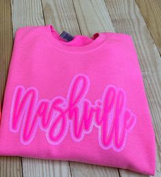 Neon pink sweatshirt with a glitter and puff Nashville script design.  Perfect just to show your love for Music City-- or for a trip to visit Nashville! Puff Vinyl Christmas Shirts, Pink Tshirt Design Ideas, Pink Casual Top With Glitter Print, Casual Pink Tops With Glitter Print, Pink Sweatshirt With Text Print For Spring, Pink Text Print Sweatshirt For Spring, Pink Glitter Print Tops For Spring, Casual Pink T-shirt With Glitter Print, Pink Long Sleeve Sweatshirt With Lettering