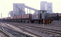 a train is traveling down the tracks in front of some industrial buildings and smokestacks