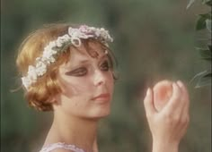 a woman with flowers in her hair holding an apple