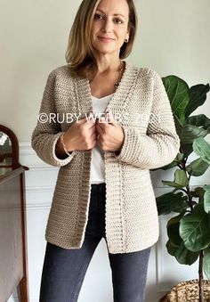 a woman standing in front of a potted plant wearing a cardigan sweater and jeans