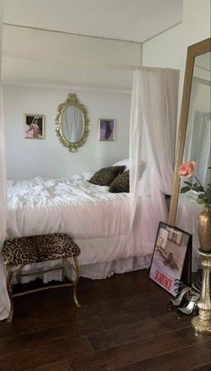 a white bed sitting next to a mirror on top of a wooden floor