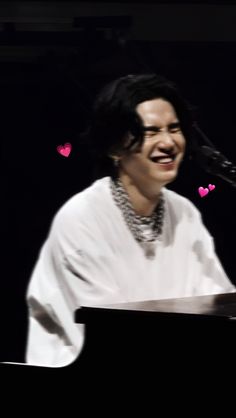 a man that is sitting in front of a piano with hearts on the wall behind him