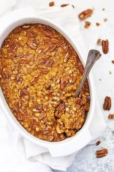 a white bowl filled with granola on top of a table next to pecans