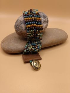 This beautiful One- of- a -Kind southwest style beaded bracelet is adorned with beautiful Picasso beads of varying colors of gold,  turquoise blue, smoky blue, brown, soft green, and burgundy.  The larger beads are 4 m. m.  Bohemian mix Opaque Picasso . The small ones are size 6 Aged Striped Czech Glass Rocaille seed beads.  The ends of the bracelet are finished with tan leather with a bronze southwest style button.  This bracelet is 7 inches long and 1 inch wide. This bracelet will fit 6-7 inch inch wrist .   I hope that you will love this very stylish bracelet!   ENJOY! Earthy Turquoise Bracelets For Festival, Bohemian Turquoise Beaded Bracelets With Wooden Beads, Artisan Beaded Multicolor Wrap Bracelet, Bohemian Beaded Cuff Bracelet, Artisan Multicolor Beaded Wrap Bracelet, Turquoise Beaded Bracelets With Wooden Beads, Bohemian Festival Cuff Bracelet With Round Beads, Bohemian Cuff Bracelet With Round Beads For Festivals, Bohemian Hand-strung Brown Beads