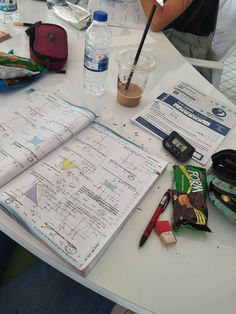 an open notebook sitting on top of a white table covered in notes and pencils