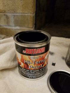 a can of paint sitting on top of a white cloth next to a metal cup