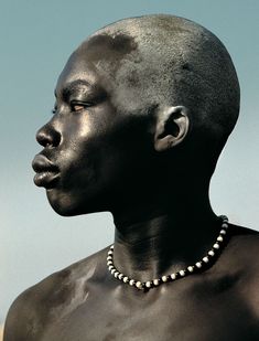 a man with no shirt on wearing a beaded necklace and standing in front of a blue sky