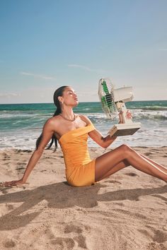 a woman sitting on the beach with a fan in her hand and looking up into the sky