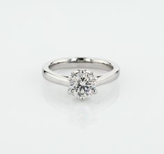 a white gold engagement ring with a round brilliant cut diamond in the center, on a plain surface